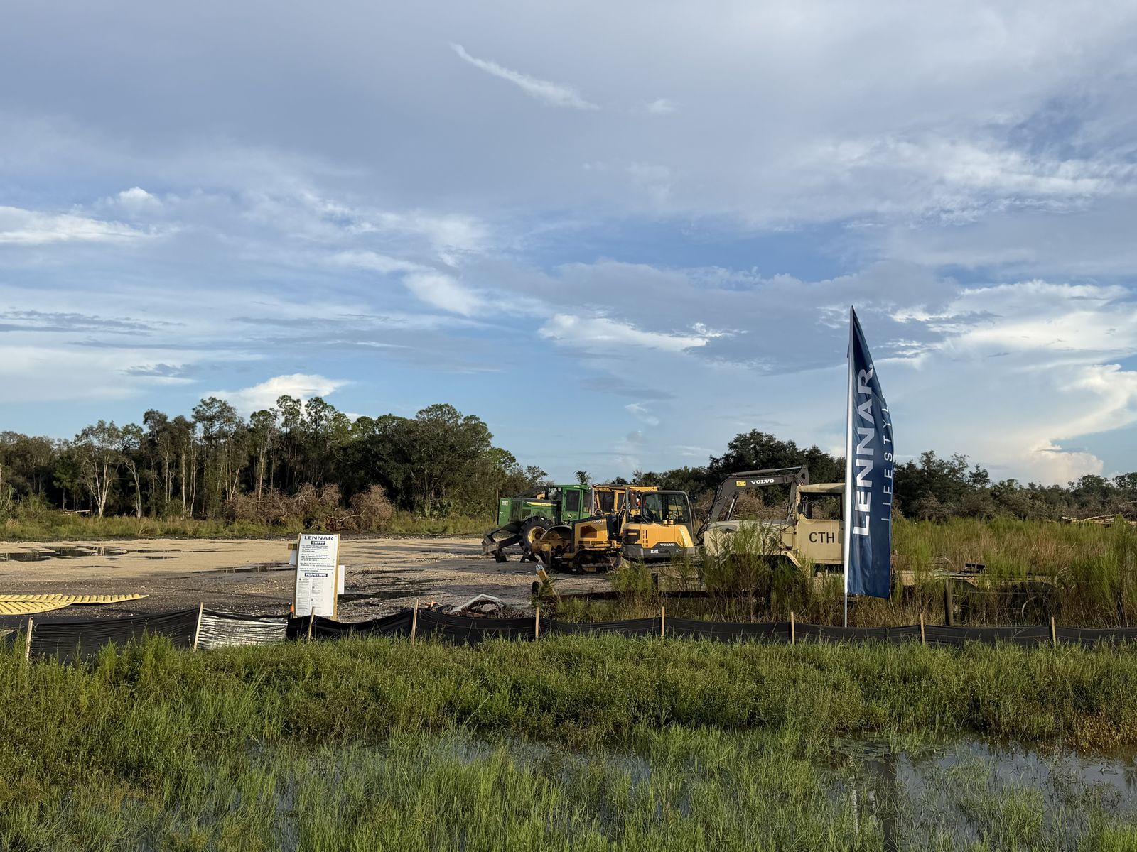 Equipment and a Lennar flag behind the silt fence. Photo: Fernando Daza, October 11, 2026.